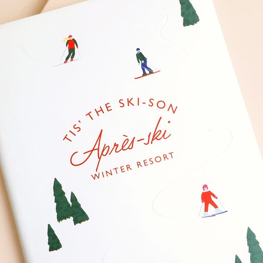 Close up of ski resort illustration and Tis the ski-son red lettering on cover