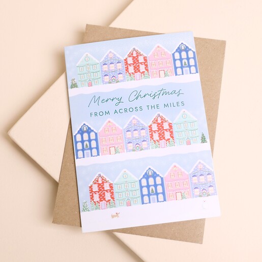 Illustrated Christmas greetings card with snowy townhouses resting on a brown kraft envelope