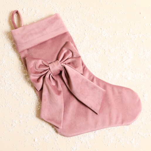 Pink velvet Christmas stocking with a large statement bow on a festive background