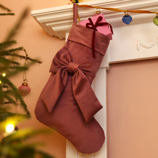 Pink velvet stocking filled with a present hanging beside a lit Christmas tree