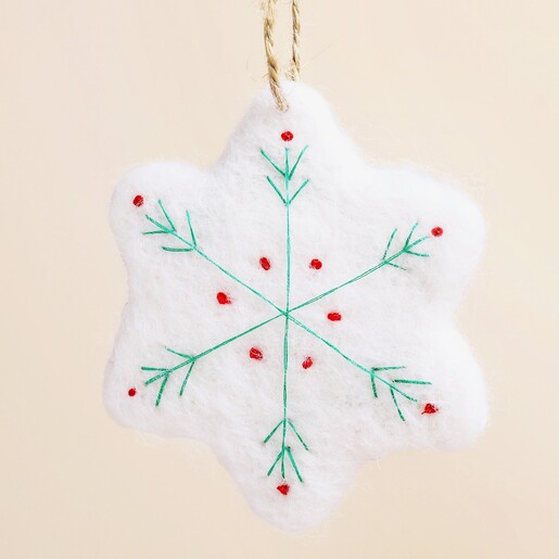 Close-up of white felt Christmas ornament featuring stitched green and red snowflake