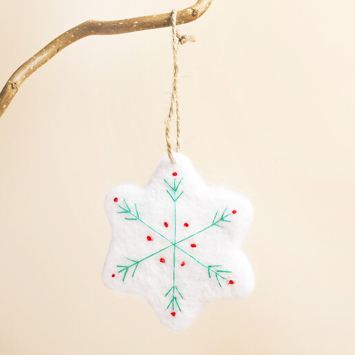 White felt snowflake decoration with green embroidery hanging from a branch