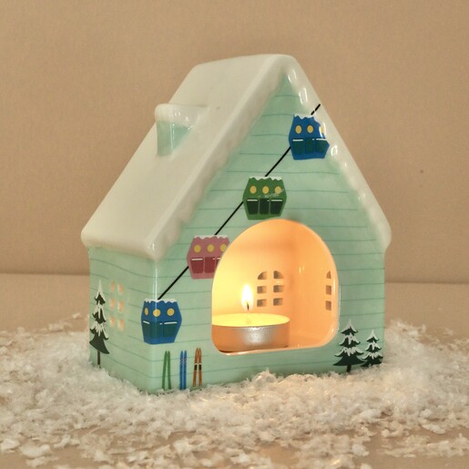 Back of ceramic ski chalet tealight holder illuminated by a lit tealight candle