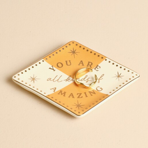 Diamond shaped ochre and cream ceramic trinket dish holding a gold ring