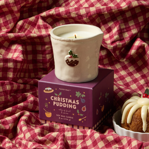 Paddywax Christmas candle atop gift box on red gingham fabric with festive bundt cake