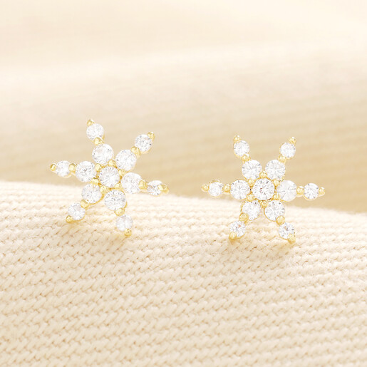 Pair of gold crystal snowflake stud earrings resting on a textured cream fabric