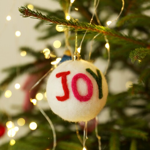 White felt Christmas bauble hanging from a branch with colourful JOY lettering.