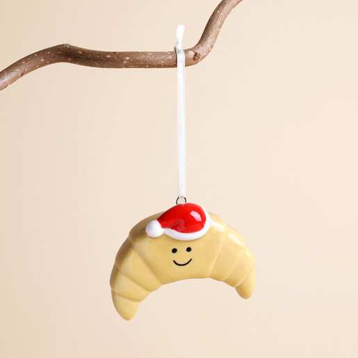 Ceramic smiling croissant hanging decoration wearing a red Santa hat on a branch