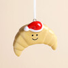 Close-up of glazed ceramic smiling croissant ornament wearing a red Santa hat