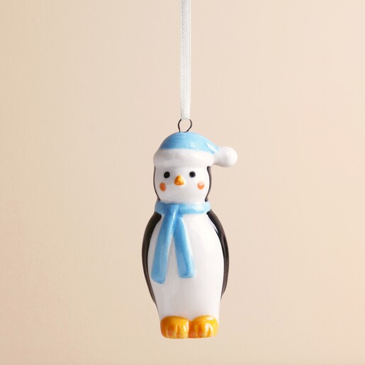 Close-up of glossy ceramic penguin decoration wearing a blue bobble hat and matching scarf