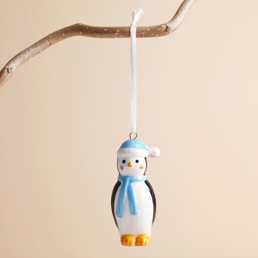 Ceramic chilly penguin decoration hanging from a wooden branch on a neutral background