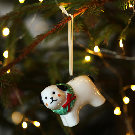 Ceramic Christmas dog tree decoration hanging on fairy-lit pine tree branches