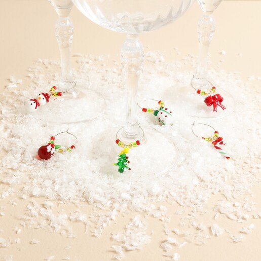 Six beaded Christmas wine glass charms attached to stems of glasses on fake snow.