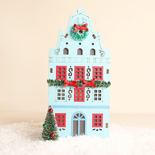 Blue wooden Dutch townhouse light decoration with festive wreath and tree in snow