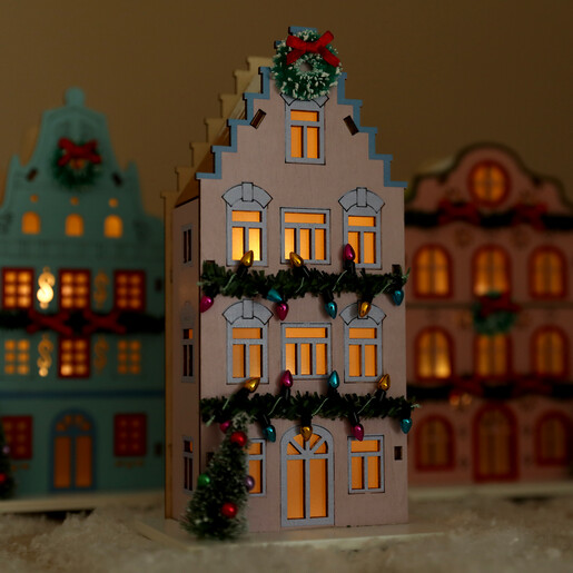 Lilac wooden LED house glowing warmly in a dim room with festive houses behind