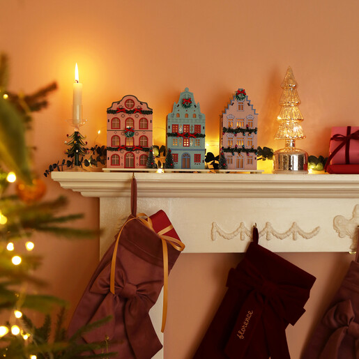 Festive mantelpiece styled with pastel wooden townhouse lights, candles and stockings