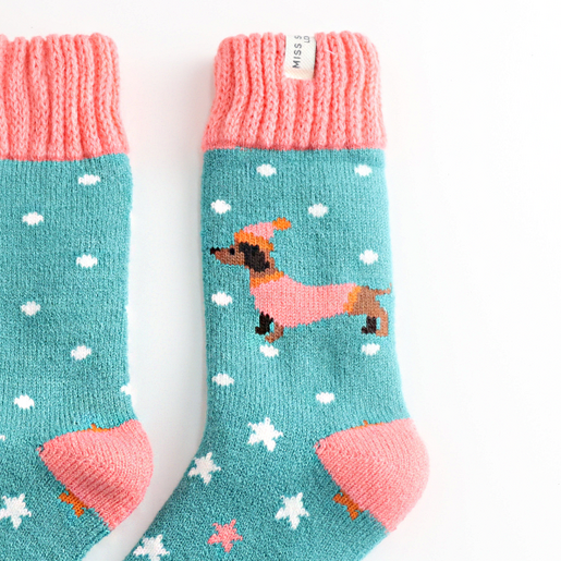 Close-up of teal knitted socks featuring a dachshund in a winter hat and jumper.