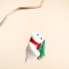 Side view of felt polar bear decoration with red scarf holding mini Christmas tree