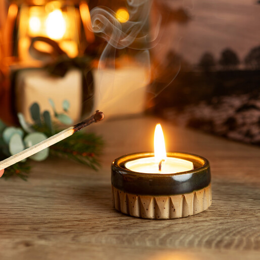 Lit scented tea light candle resting inside a rustic fluted ceramic holder