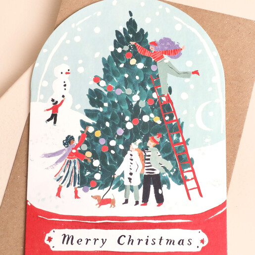Close-up of the snowglobe card illustration featuring figures decorating a Christmas tree.