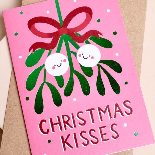 Close-up of mistletoe illustration and Christmas Kisses text on pink card