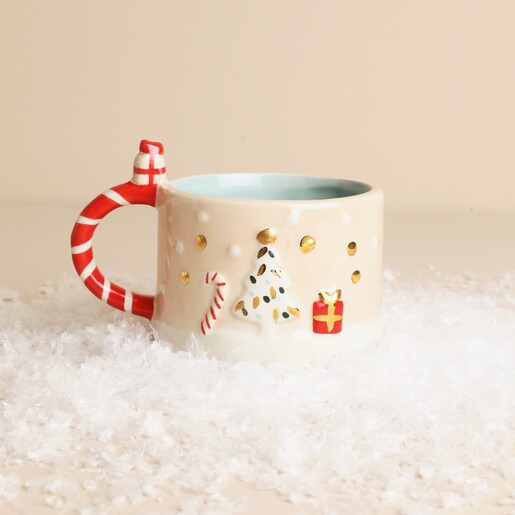 Small ceramic festive mug decorated with Christmas tree and present details on faux snow