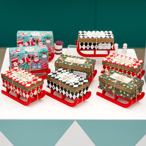 Collection of festive trivia and puzzle game boxes displayed on miniature sleighs.