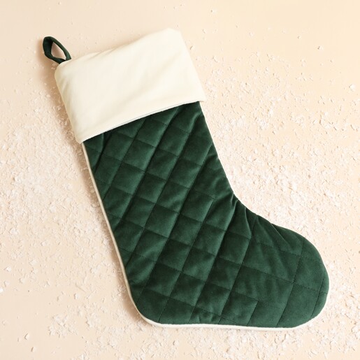 Dark green quilted velvet Christmas stocking with a cream cuff on festive snow.