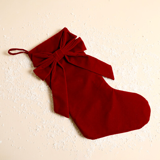 Red velvet Christmas stocking with a large bow against a snowy backdrop