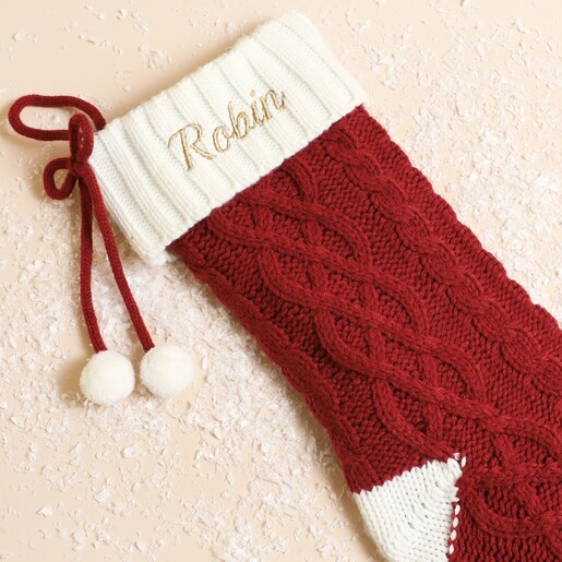 Close-up of personalised red knitted Christmas stocking with cream embroidered cuff and pom-poms