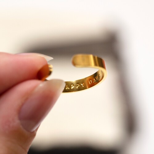 person holding gold hand stamped ring between fingers