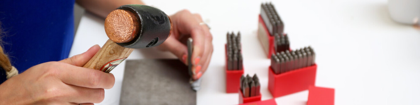 a personalisation team member hand stamping a piece of jewellery with a stamp and small hammer