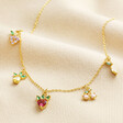 Colourful Crystal Fruit Charm Necklace in Gold laid on top of beige coloured material