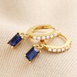 Blue Stone and Crystal Charm Huggie Hoop Earrings in Gold on Beige Fabric