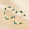Green Enamel Striped Heart Hoop Earrings in Gold on Beige Fabric