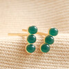 Green Stone Bar Stud Earrings in Gold laid on top of beige coloured fabric