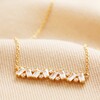 Close Up of Crystal Baguette Bar Necklace in Gold on Beige Fabric 