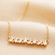 Close Up of Crystal Baguette Bar Necklace in Gold on Beige Fabric 
