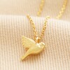 Delicate Bird Pendant Necklace in Gold on beige fabric