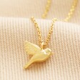 Delicate Bird Pendant Necklace in Gold on beige fabric